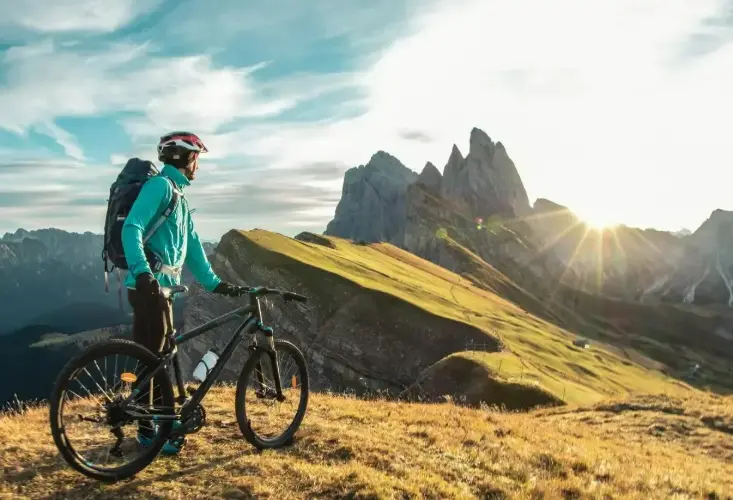 Jeune homme en vélo faisant une pause pour admirer un paysage montagneux baigné par la lumière du soleil