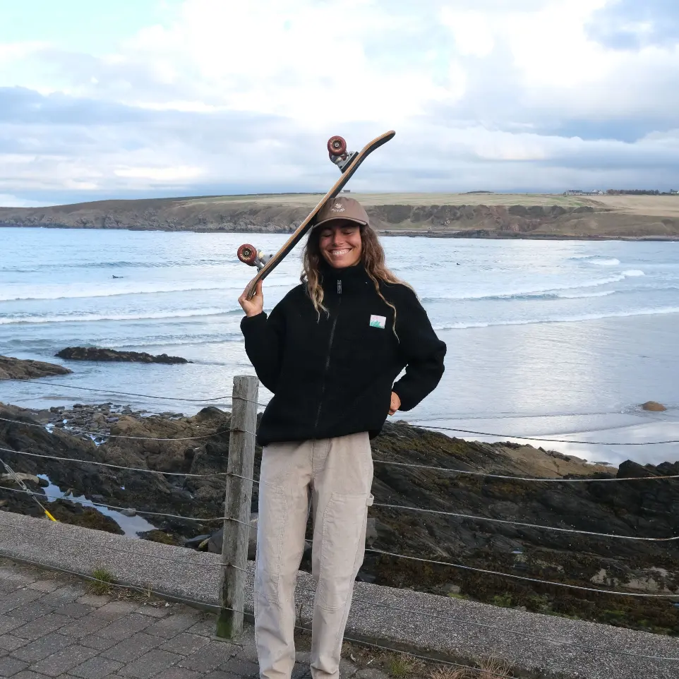Jeune femme tenant un skate au dessus de sa tête avec en arrière plan une étendue d&#39;eau