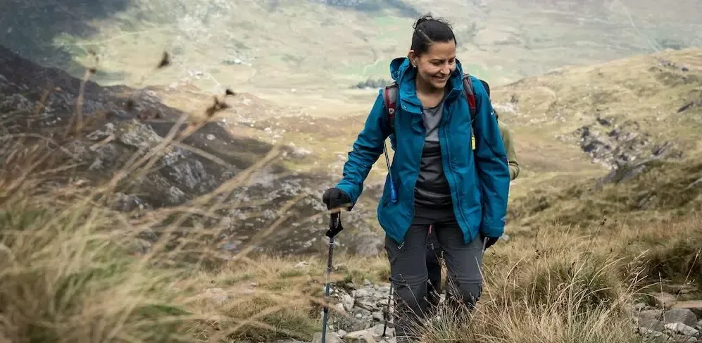 Jeune femme souriante avec ses batons de marche dans un paysage valonné
